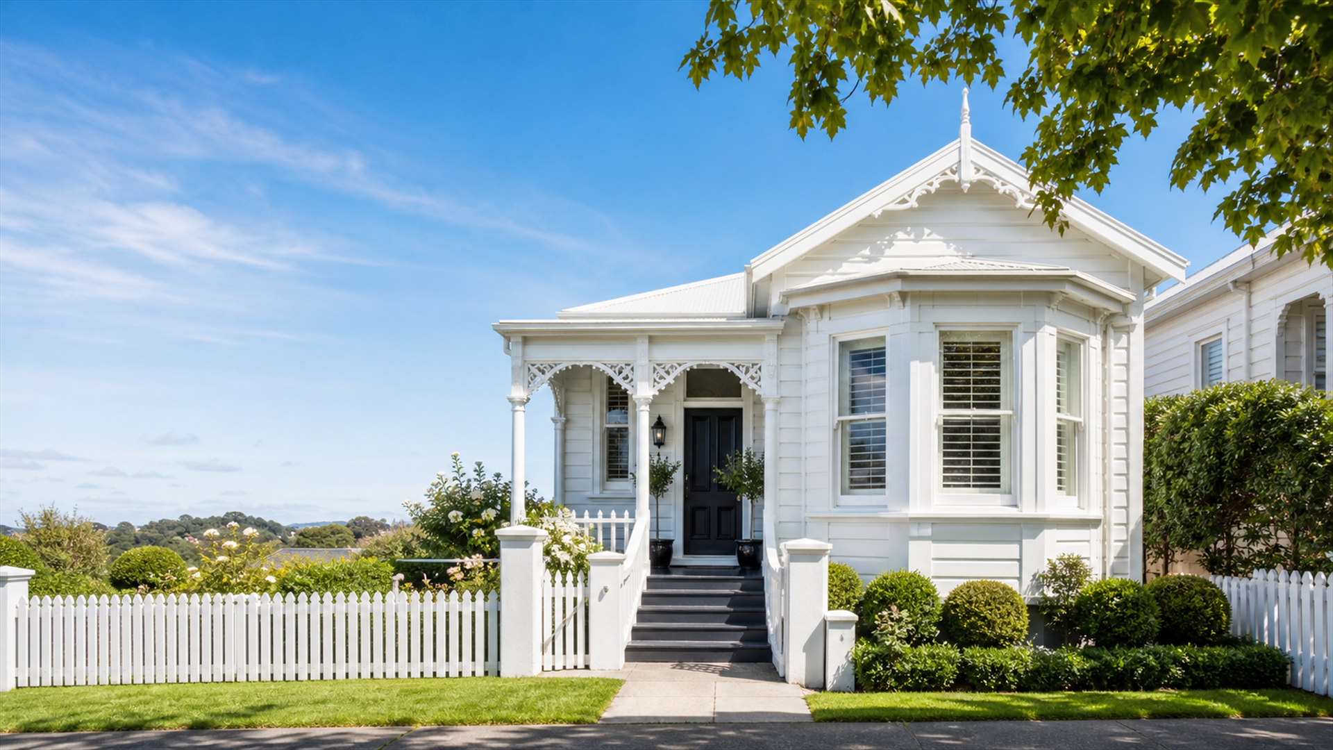 Freshly painted white Auckland villa with a wraparound porch and picket fence