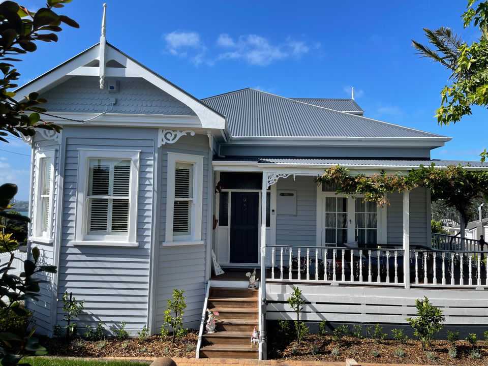 Grey weatherboard villa with white porch, freshly painted